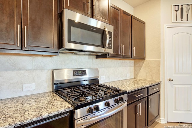 kitchen featuring dark brown cabinets, stainless steel appliances, light stone countertops, and decorative backsplash