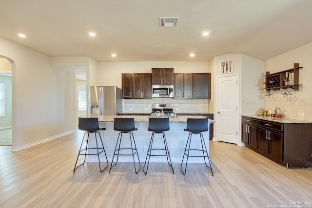 kitchen featuring appliances with stainless steel finishes, a kitchen bar, light stone countertops, and an island with sink