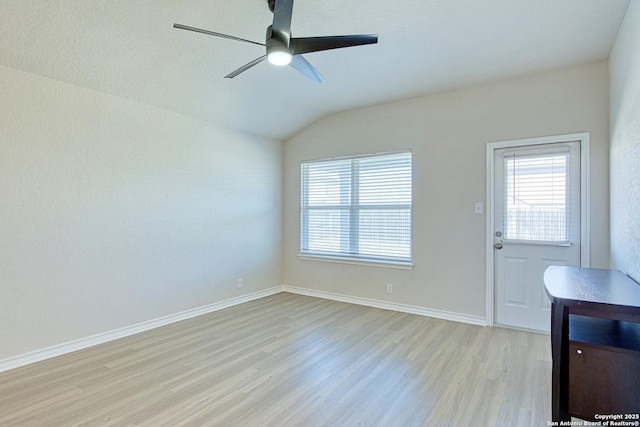 empty room with vaulted ceiling, a healthy amount of sunlight, ceiling fan, and light wood-type flooring