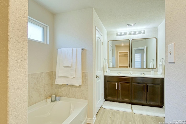 bathroom featuring vanity, a tub to relax in, wood-type flooring, and a textured ceiling