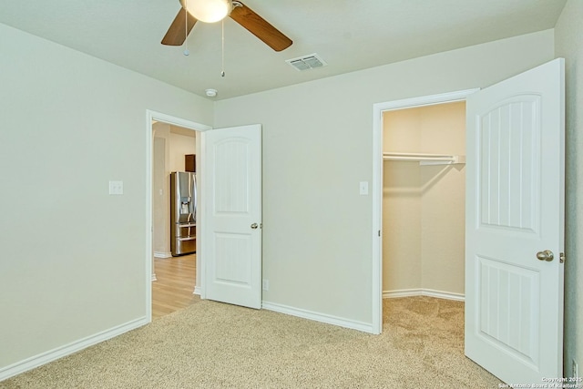 unfurnished bedroom featuring a walk in closet, light carpet, stainless steel fridge, and ceiling fan