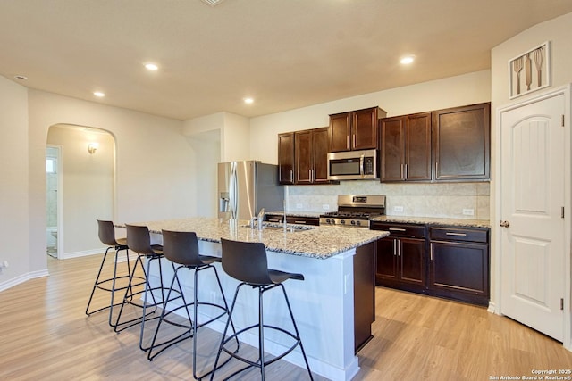 kitchen with appliances with stainless steel finishes, a kitchen island with sink, a breakfast bar, and decorative backsplash