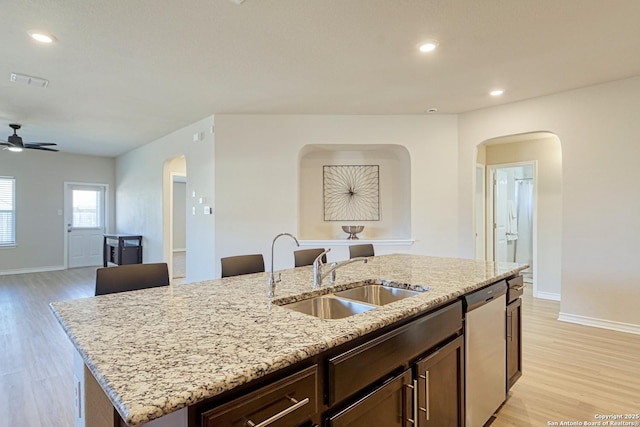 kitchen featuring light stone counters, sink, dishwasher, and an island with sink