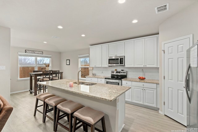 kitchen with stainless steel appliances, a kitchen island with sink, sink, and white cabinets