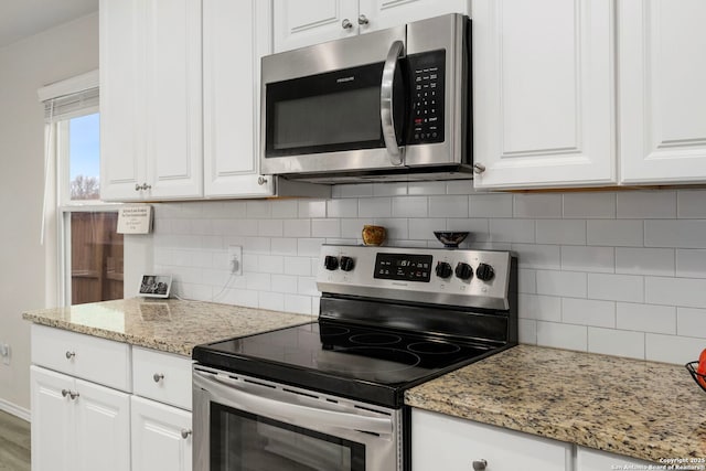 kitchen with white cabinetry, stainless steel appliances, light stone countertops, and backsplash