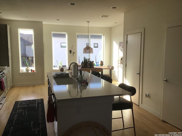 kitchen featuring pendant lighting, sink, a kitchen island with sink, a wealth of natural light, and light hardwood / wood-style floors