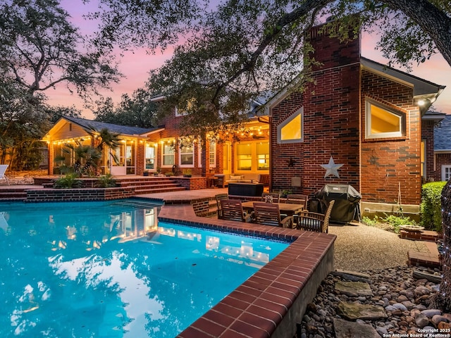 pool at dusk with a grill, an outdoor living space, and a patio