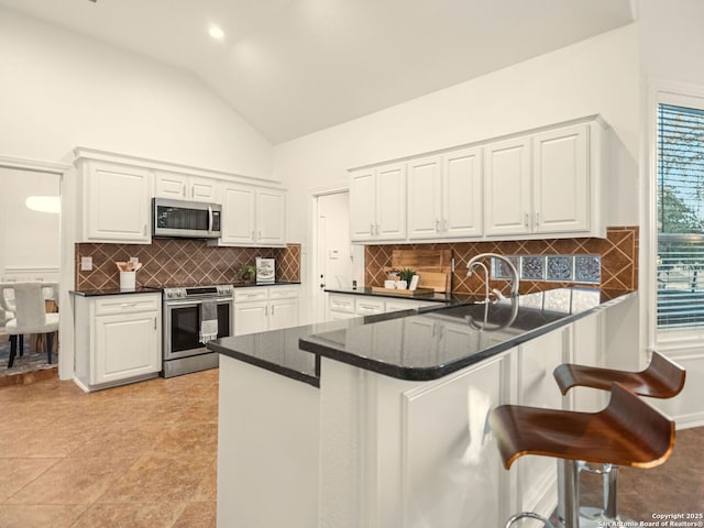 kitchen with lofted ceiling, appliances with stainless steel finishes, white cabinets, and kitchen peninsula