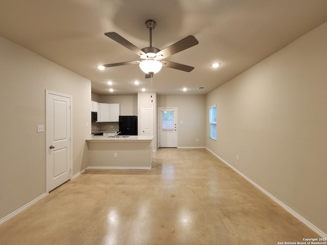 kitchen featuring sink, white cabinetry, black refrigerator, kitchen peninsula, and light stone countertops