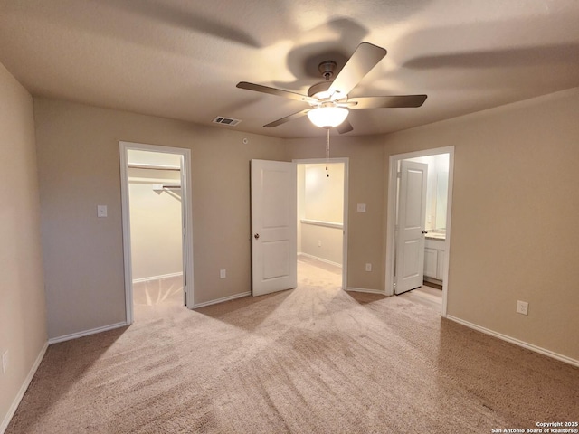 unfurnished bedroom with ceiling fan, ensuite bathroom, light carpet, a spacious closet, and a closet