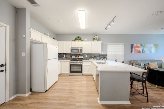 kitchen featuring sink, appliances with stainless steel finishes, white cabinetry, a kitchen bar, and kitchen peninsula