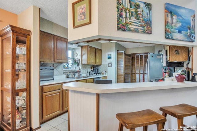 kitchen with a kitchen bar, sink, light tile patterned floors, stainless steel fridge, and kitchen peninsula