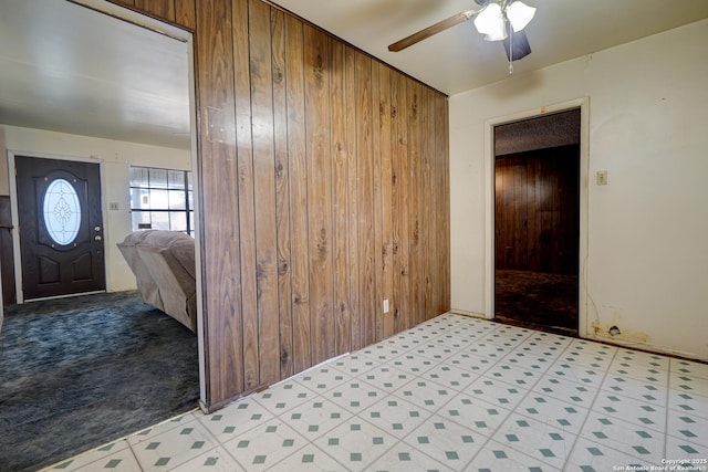 foyer entrance featuring ceiling fan, light carpet, and wooden walls