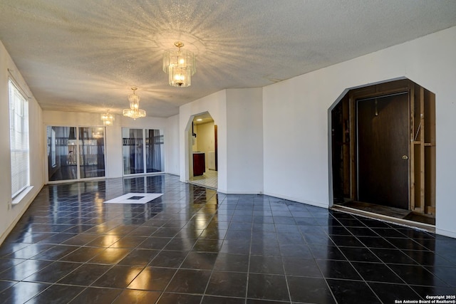 tiled spare room with a textured ceiling and a chandelier