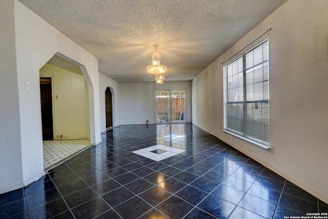 spare room featuring an inviting chandelier, dark tile patterned flooring, and a textured ceiling