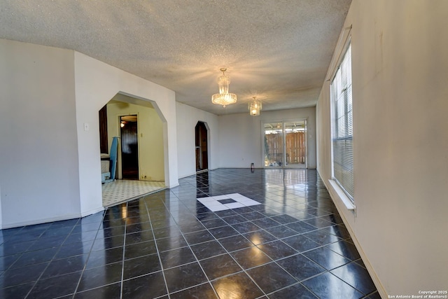 tiled empty room with a notable chandelier and a textured ceiling