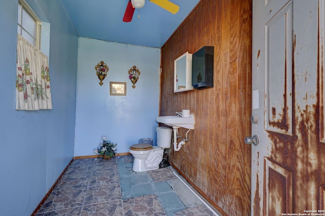 bathroom featuring ceiling fan, sink, wooden walls, and toilet