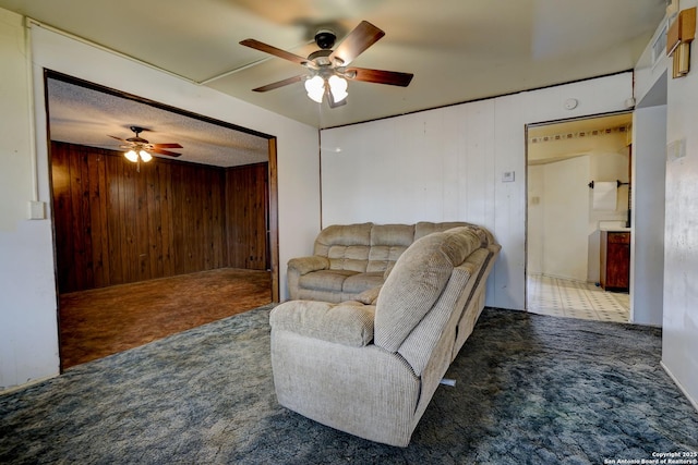 living room featuring ceiling fan, carpet floors, a textured ceiling, and wood walls