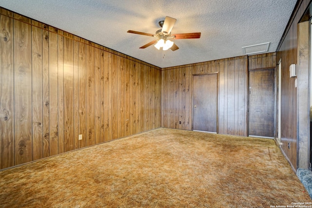 spare room featuring wooden walls, carpet floors, and a textured ceiling