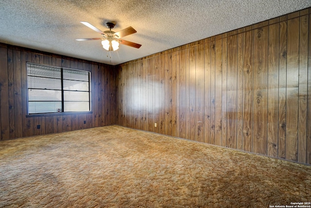 carpeted empty room featuring ceiling fan, wooden walls, and a textured ceiling