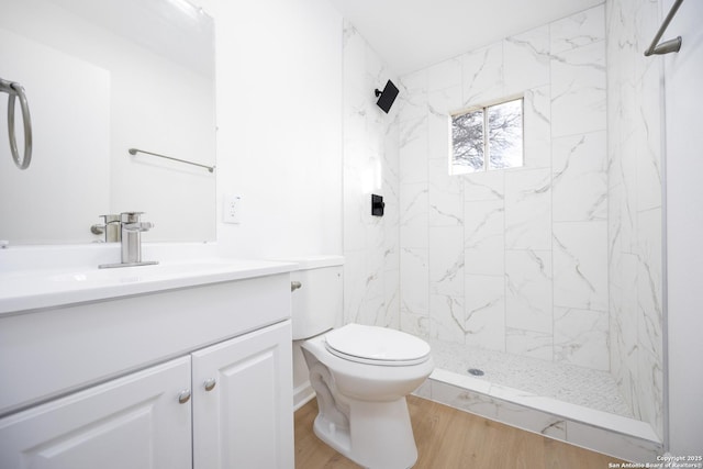 bathroom with hardwood / wood-style flooring, tiled shower, vanity, and toilet