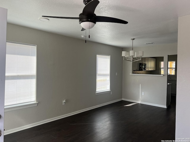 unfurnished living room with ceiling fan with notable chandelier, a textured ceiling, and dark hardwood / wood-style flooring