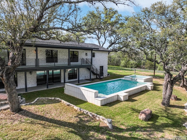 rear view of property with a balcony, a patio, a pool with hot tub, and a lawn