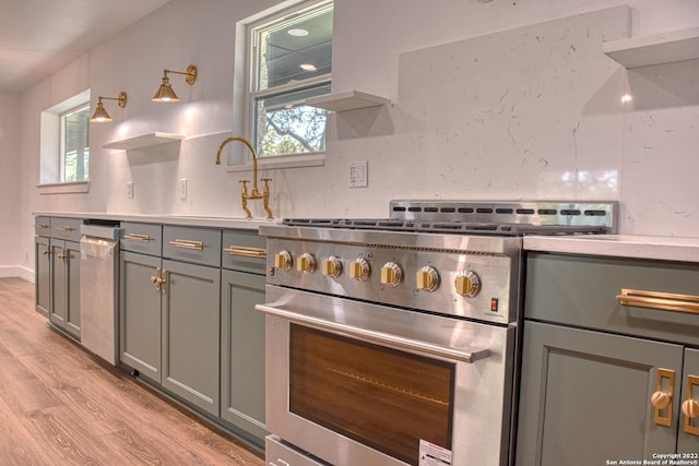 kitchen featuring sink, tasteful backsplash, light wood-type flooring, gray cabinets, and high end stainless steel range oven