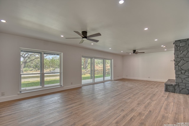 unfurnished living room with ceiling fan, a stone fireplace, and light hardwood / wood-style floors