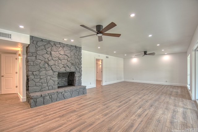 unfurnished living room with ceiling fan, a stone fireplace, and light hardwood / wood-style floors