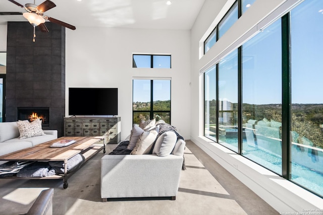 living room featuring a large fireplace, a high ceiling, a ceiling fan, and concrete flooring