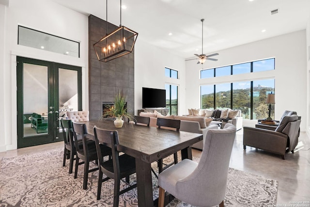 dining space with concrete flooring, a tile fireplace, recessed lighting, visible vents, and a towering ceiling