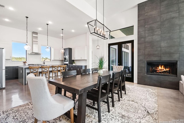 dining space featuring finished concrete floors, visible vents, a towering ceiling, and a tiled fireplace