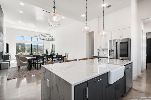 kitchen featuring a center island with sink, open floor plan, stainless steel appliances, pendant lighting, and a sink