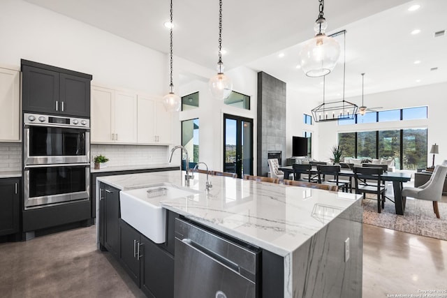 kitchen with stainless steel appliances, white cabinetry, a kitchen island with sink, and decorative light fixtures