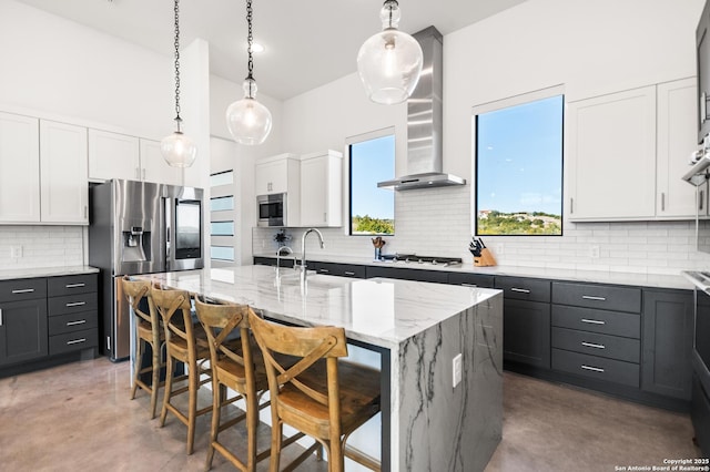 kitchen featuring wall chimney exhaust hood, an island with sink, white cabinets, and stainless steel appliances