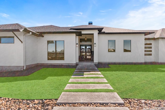 entrance to property featuring french doors, a lawn, a shingled roof, and stucco siding