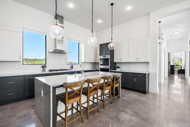 kitchen featuring hanging light fixtures, dark cabinets, a kitchen island with sink, and white cabinets