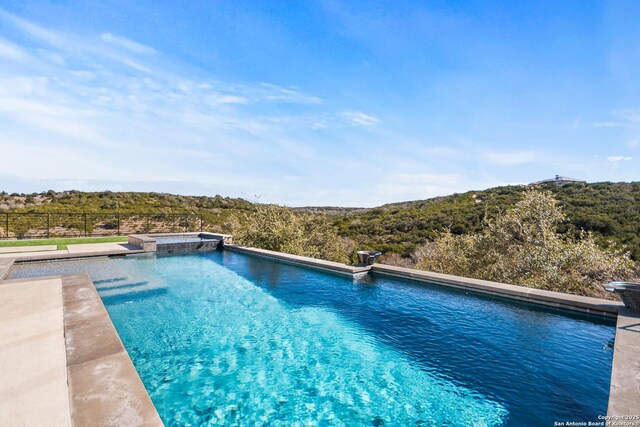 view of swimming pool with a pool with connected hot tub, fence, and a forest view