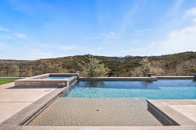 view of pool featuring a pool with connected hot tub, fence, and a view of trees