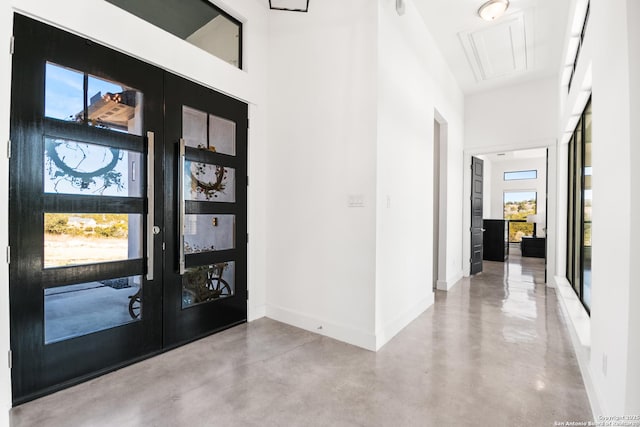 entryway featuring concrete flooring, french doors, a high ceiling, and baseboards