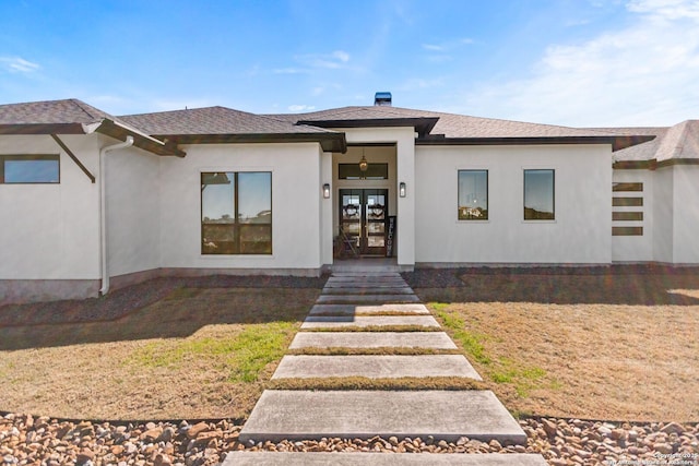 property entrance with roof with shingles, french doors, a lawn, and stucco siding