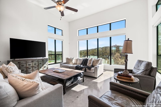 living area with a towering ceiling, ceiling fan, and concrete floors