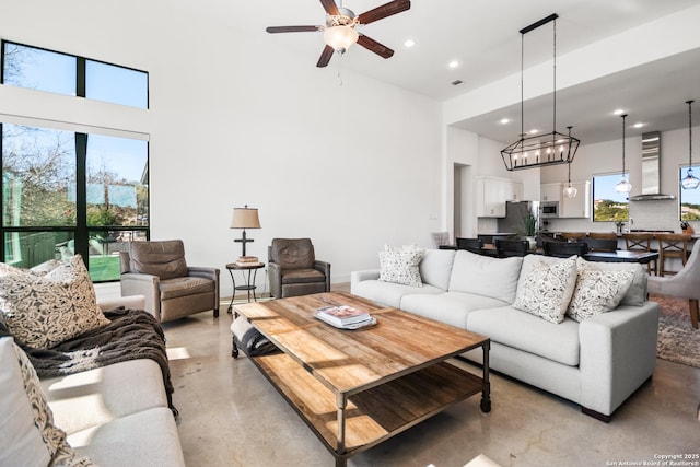 living area with finished concrete flooring, a high ceiling, ceiling fan with notable chandelier, and recessed lighting