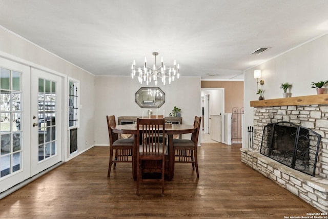 dining room with a fireplace, a chandelier, ornamental molding, dark wood-type flooring, and french doors