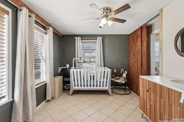 bedroom featuring light tile patterned flooring, ceiling fan, and a nursery area