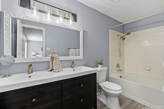 full bathroom featuring hardwood / wood-style flooring, tiled shower / bath combo, vanity, a textured ceiling, and toilet