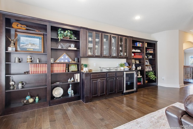 bar with wine cooler, dark brown cabinetry, and dark wood-type flooring