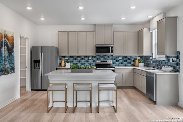 kitchen with sink, appliances with stainless steel finishes, gray cabinets, a kitchen island, and light hardwood / wood-style floors