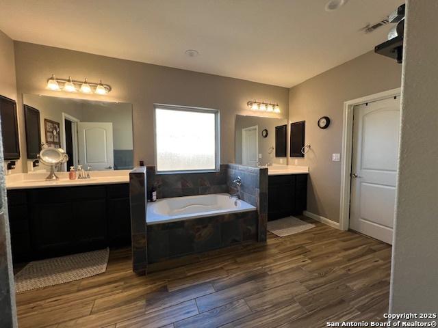 bathroom featuring hardwood / wood-style flooring, vanity, and a relaxing tiled tub